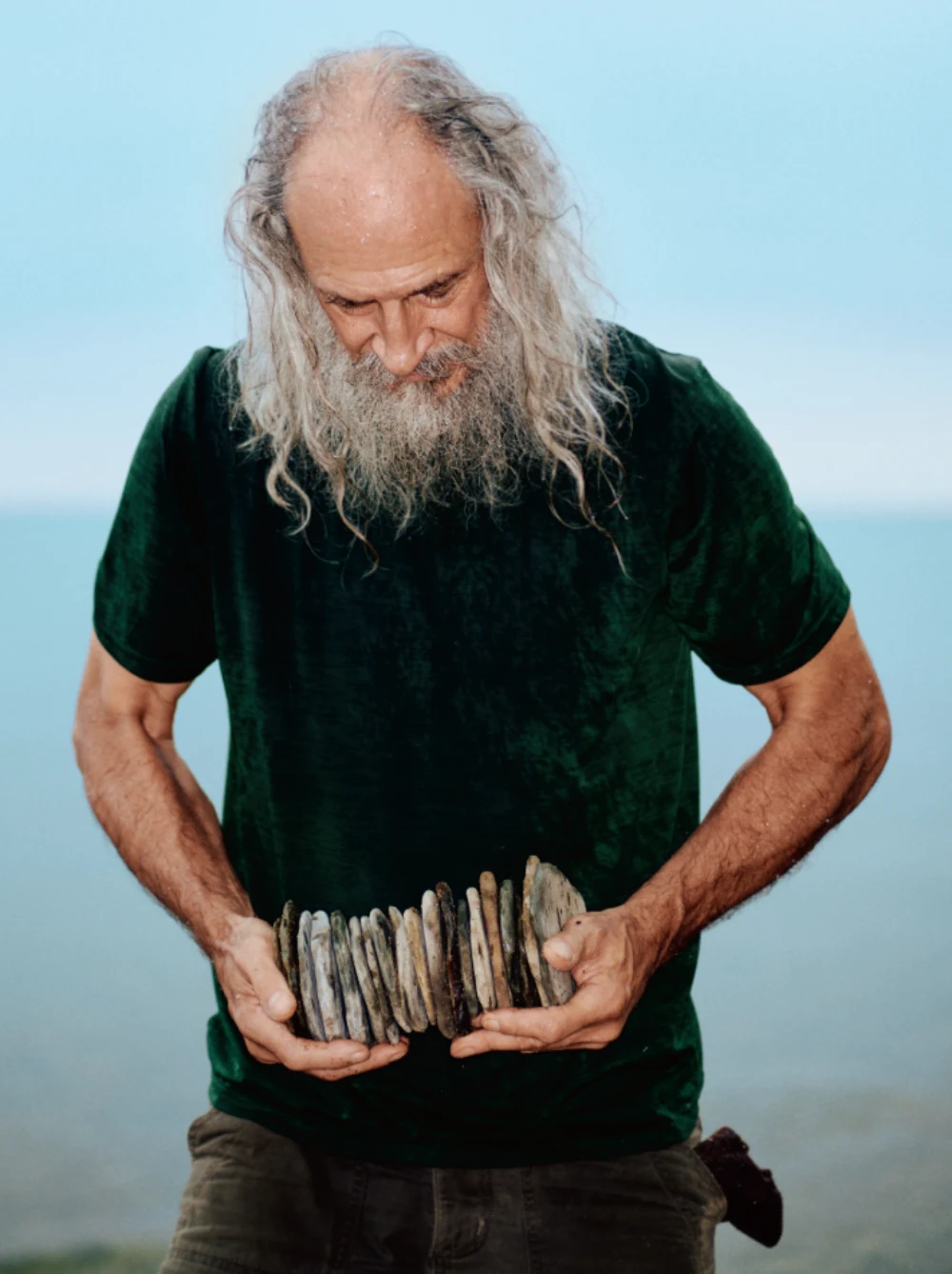 Un homme à la longue barbe grise tient une pile de pierres plates