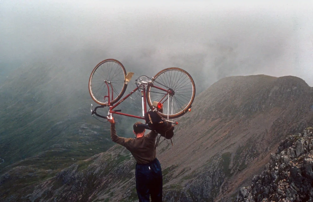 Un cycliste porte son vélo à bout de bras sur une crête dans la brume