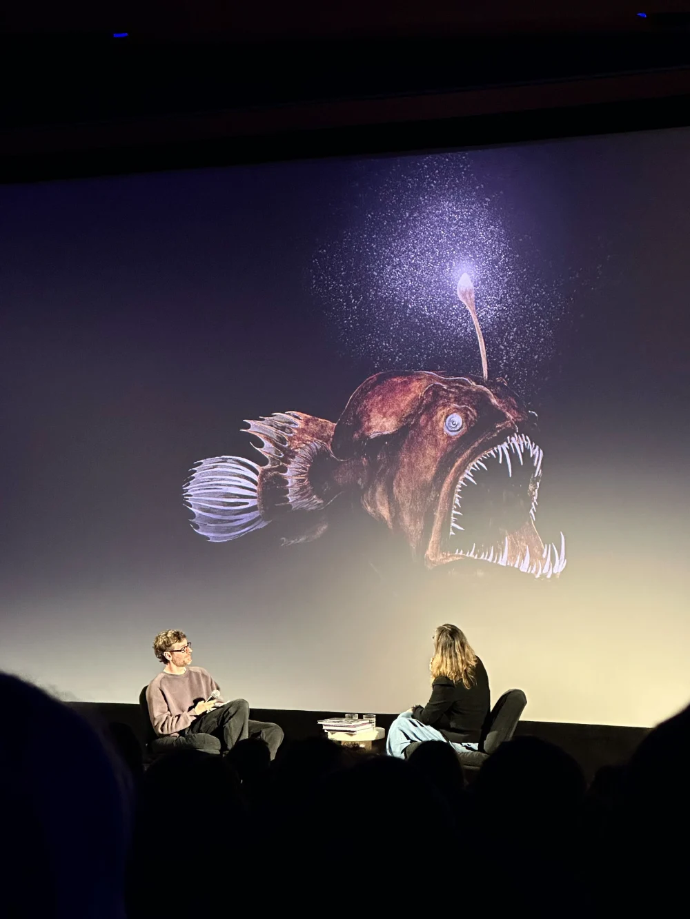 Une rencontre sur scène, deux personnes assises sous la projection d’un poisson des abysses